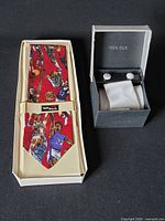 Red silk sport motif tie in original tray next to boxed white silk tie set