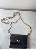 Full view of black Coach wallet with attached gold-tone chain strap