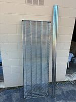 Stack of six chrome wire shelves leaning against wall with four matching chrome poles