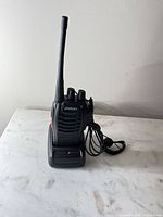 Front view of Pxton radio on charging dock with wired earpiece visible