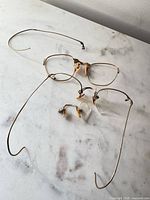 Overall view of gold-tone rimless pince-nez eyeglasses showing cable temples and broken lenses
