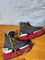Pair of Bauer Charger skates with red blade guards on wooden surface