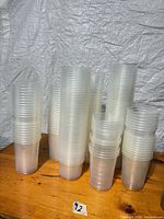 Multiple tall stacks of clear plastic cups on wood surface