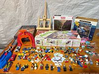 Overview of all items on table: LEGO bricks, puzzles, board game, easel, cars, doll