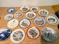 Fifteen of the souvenir plates laid out, showing range of landmark designs and colour schemes
