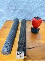 Pair of long dark gray perforated metal finch feeders and red hummingbird feeder on wooden surface