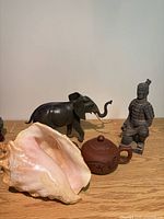 Group shot showing all four items: conch shell, teapot, elephant figurine, warrior figurine