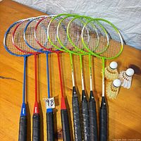 Eight rackets lined on table with three shuttlecocks