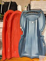 Red and blue plastic sleds side by side