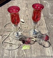 Two electric cranberry hurricane lamps with clear inserts and cords