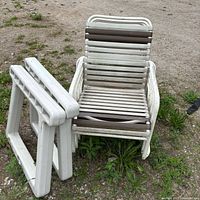 Stacked white tubular metal armchairs with brown and white plastic straps, two white plastic table legs leaning in front
