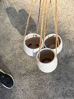 Three white ceramic hanging planters suspended by jute cords
