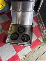 Cooktop open showing three coil burners and stainless cover