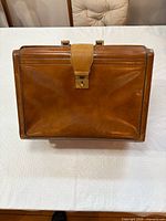 Front view of brown leather suitcase showing strap lock and handle