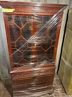 Front view of tall wooden cabinet wrapped in plastic
