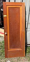 Full view of solid wood single-panel door standing upright outdoors