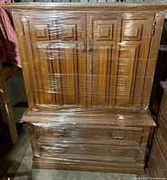 Front view of wood dresser showing doors and drawers wrapped in plastic