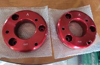 Two red anodized billet aluminum spacers top view showing bolt holes marked A and OUT