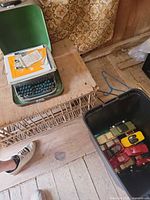 Overview of lot including typewriter in case and plastic bin nearby