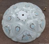 Top view of frosted glass ceiling shade showing etched geometric and blue floral pattern, central hole, brass finial nearby