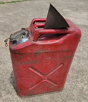 Front angled view of red metal jerry can, funnel inserted in handle