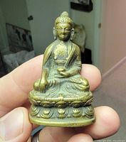 Front view of brass Buddha figurine showing details of face, robe and lotus base