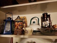 Shelf view showing lanterns, stein, kettle, glass bowl, creamer