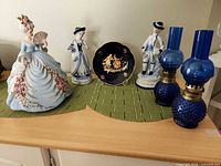 Group shot of all items: two blue hobnail oil lamps, three porcelain figurines, cobalt plate