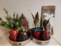 overall view of both galvanized trays containing potted faux plants, red lanterns, resin figurine; wooden moose sign behind