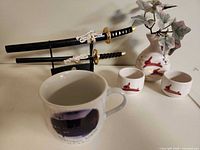 Overall lot view showing swords on stand, mug, vase with plant, and two cups