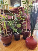 Group shot of all four red ceramic planters with artificial plants and saucers