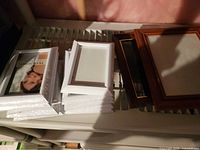 Stack of white shrink-wrapped frames beside two wood-tone frames