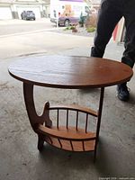 Full view of brown veneer side table showing oval top and magazine rack