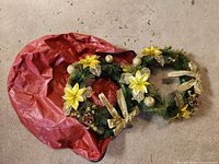 Pair of decorated artificial Christmas wreaths beside red storage bag