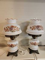 Front view of both milk glass hurricane lamps showing floral shades and metal bases
