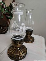 Both lamps showing glass chimneys with floral etching and antique brass bases