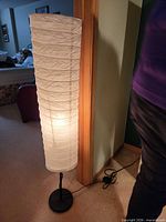 Full view of lit floor lamp showing white paper shade and black base