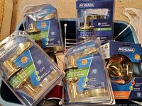 Bin with five packaged Schlage brass hardware pieces: four lever sets and one deadbolt