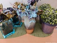 Overall view showing ceramic vase with hydrangeas and two teal glass vases with foliage