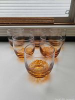Front view of six amber speckled tumblers on white surface