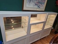 Front view of white glass-door curio cabinet showing three main sections, glass shelves, mirrored back and interior lighting