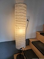 Full view of illuminated floor lamp showing paper shade, metal stand and base