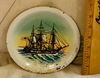 Front view of enamel metal plate showing ship illustration and ruler for scale