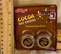Front view of sealed Cocoa Rice Krispies lip gloss package with ruler for scale