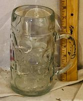 Front view of clear dimpled glass beer mug beside ruler