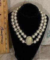 Full view of double-strand faux pearl necklace on display bust with ruler for scale