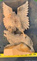 Front view of carved eagle atop wolf on base with measuring tape for scale
