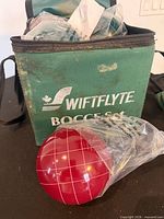 Green Swiftflyte carry case with one red bocce ball in plastic wrap