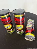 Three sealed cans of Penn Championship tennis balls standing and lying on black surface