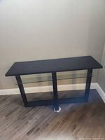 Front view of black engineered wood console table with clear glass shelf